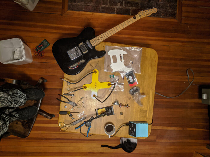 Skunk's elecric guitar laid out on the table, with a soldering iron and a bunch of tools.